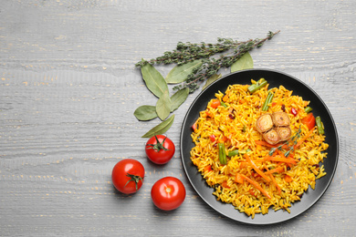 Photo of Tasty rice pilaf with vegetables on grey wooden table, flat lay