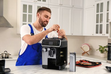 Repairman with screwdriver fixing coffee machine at table in kitchen