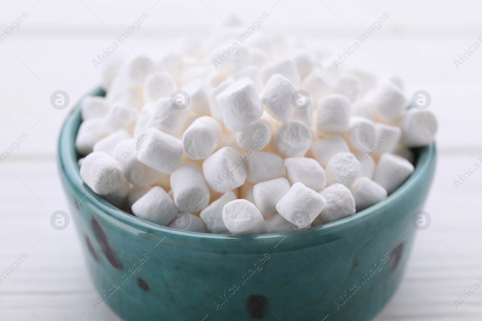 Photo of Bowl with delicious marshmallows on white table, closeup