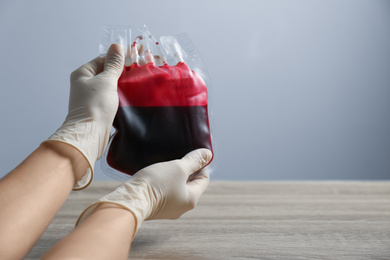 Photo of Woman holding blood for transfusion at wooden table, closeup with space for text. Donation concept