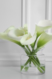 Photo of Beautiful calla lily flowers in glass vase on white table