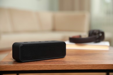 One black portable bluetooth speaker on wooden table indoors, space for text. Audio equipment