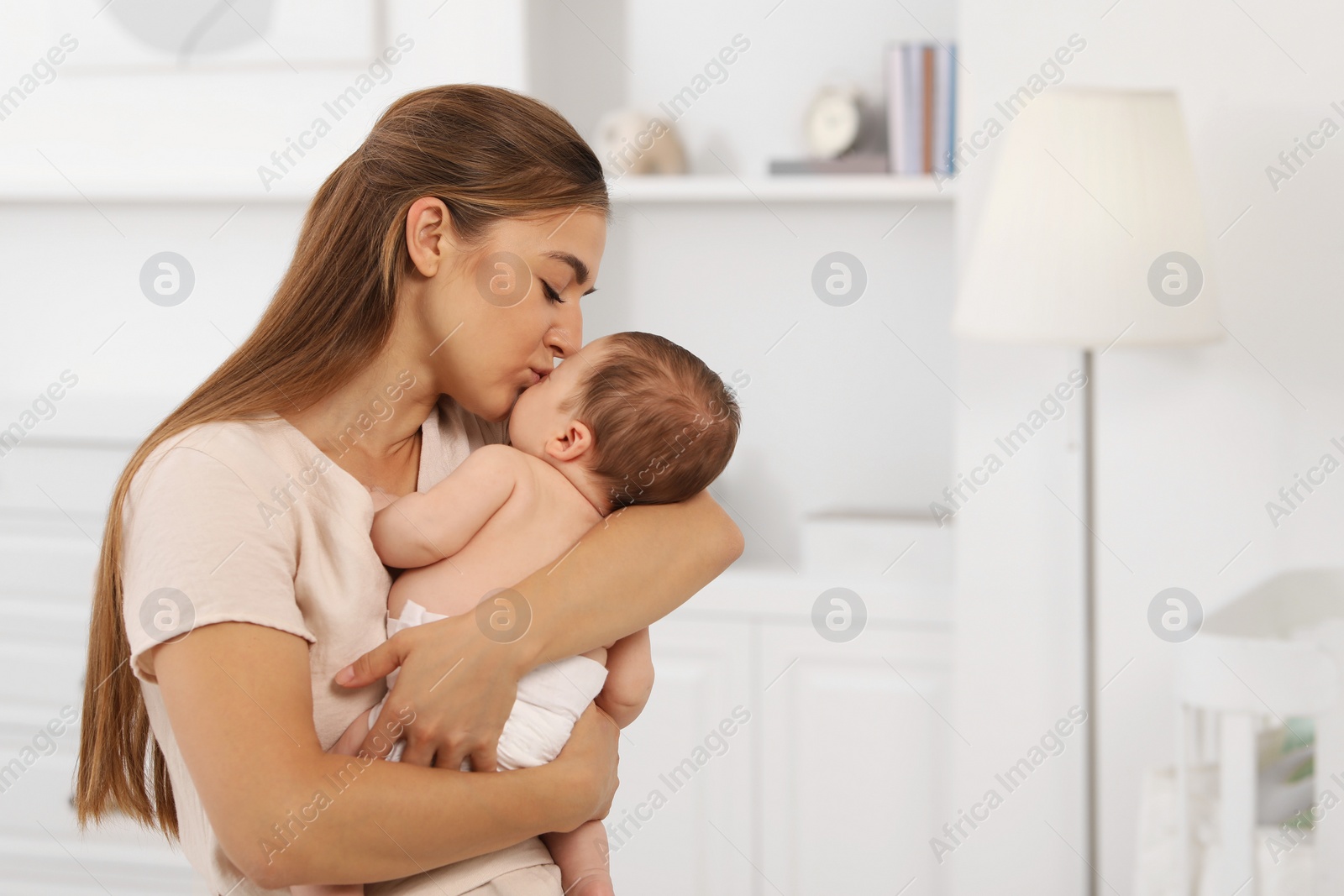 Photo of Mother kissing her cute newborn baby indoors, space for text