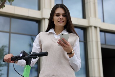 Photo of Businesswoman with modern kick scooter using smartphone on city street, low angle view
