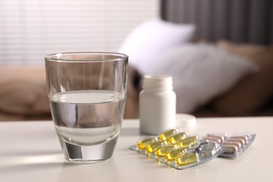 Photo of Glass of water, different pills in blisters and medical bottle on white table indoors