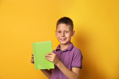 Image of Happy little boy with book on yellow background