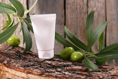 Tube of cream, olives and leaves on log near wooden wall