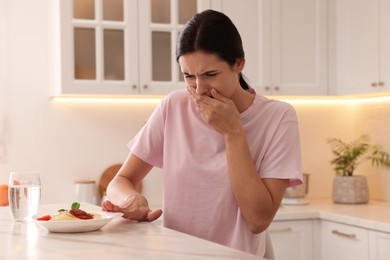 Photo of Young woman feeling nausea while seeing food at table in kitchen