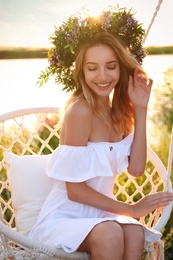 Photo of Young woman wearing wreath made of beautiful flowers on swing chair outdoors