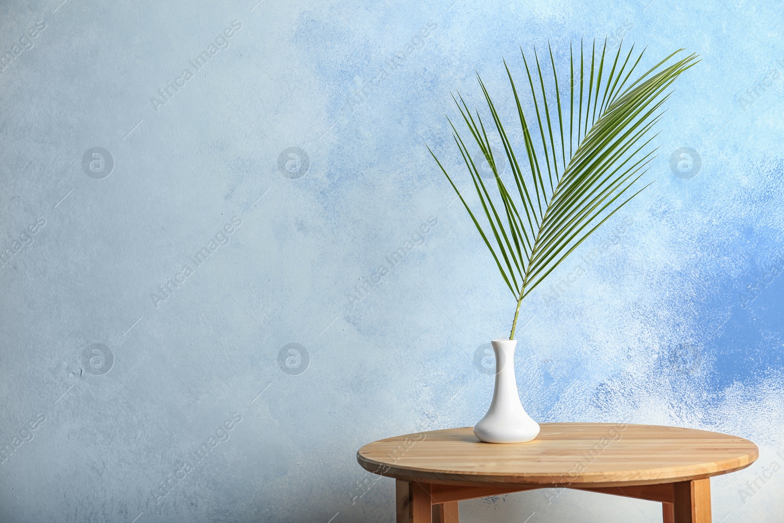 Photo of Vase with tropical Date palm leaf on table. Space for text