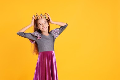 Photo of Cute girl in dress and golden crown with gems on yellow background, space for text. Little princess