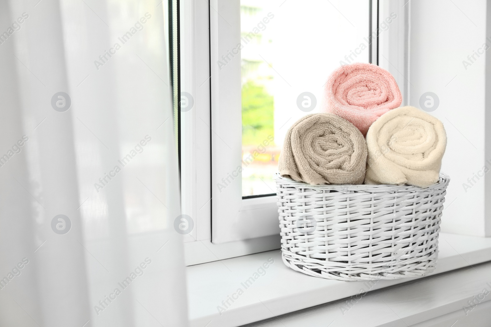Photo of Basket with clean soft towels on window sill. Space for text