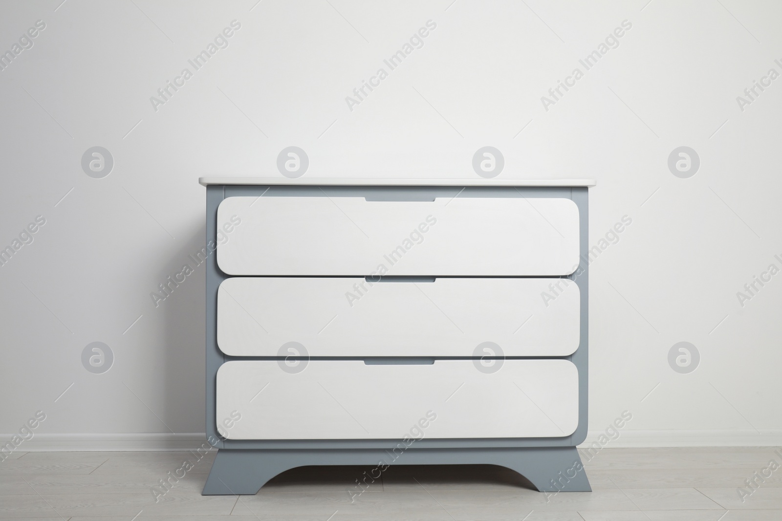 Photo of Modern wooden chest of drawers at light wall