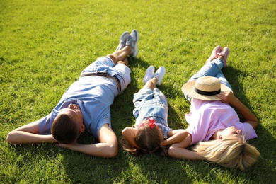 Photo of Happy parents with their child lying on green grass. Spending time in nature