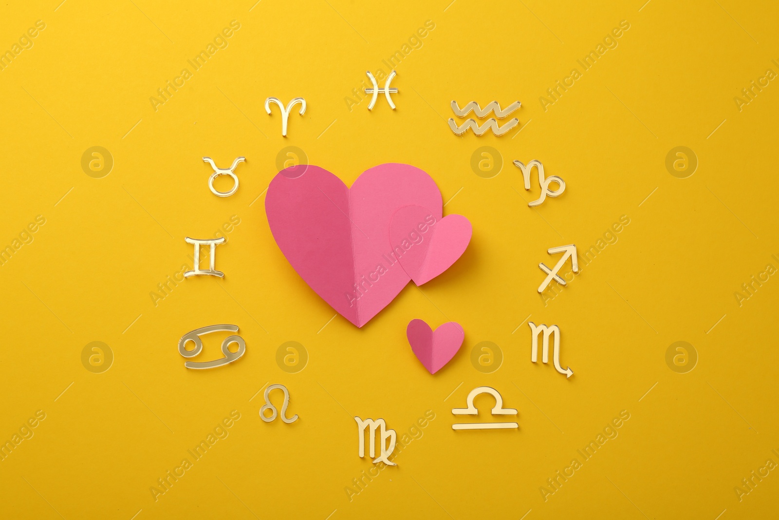Photo of Zodiac signs and pink hearts on yellow background, flat lay