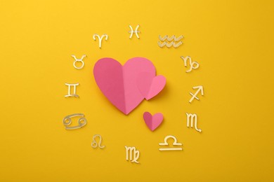 Zodiac signs and pink hearts on yellow background, flat lay