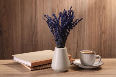 Photo of Bouquet of beautiful preserved lavender flowers, notebooks and cup of coffee on wooden table indoors