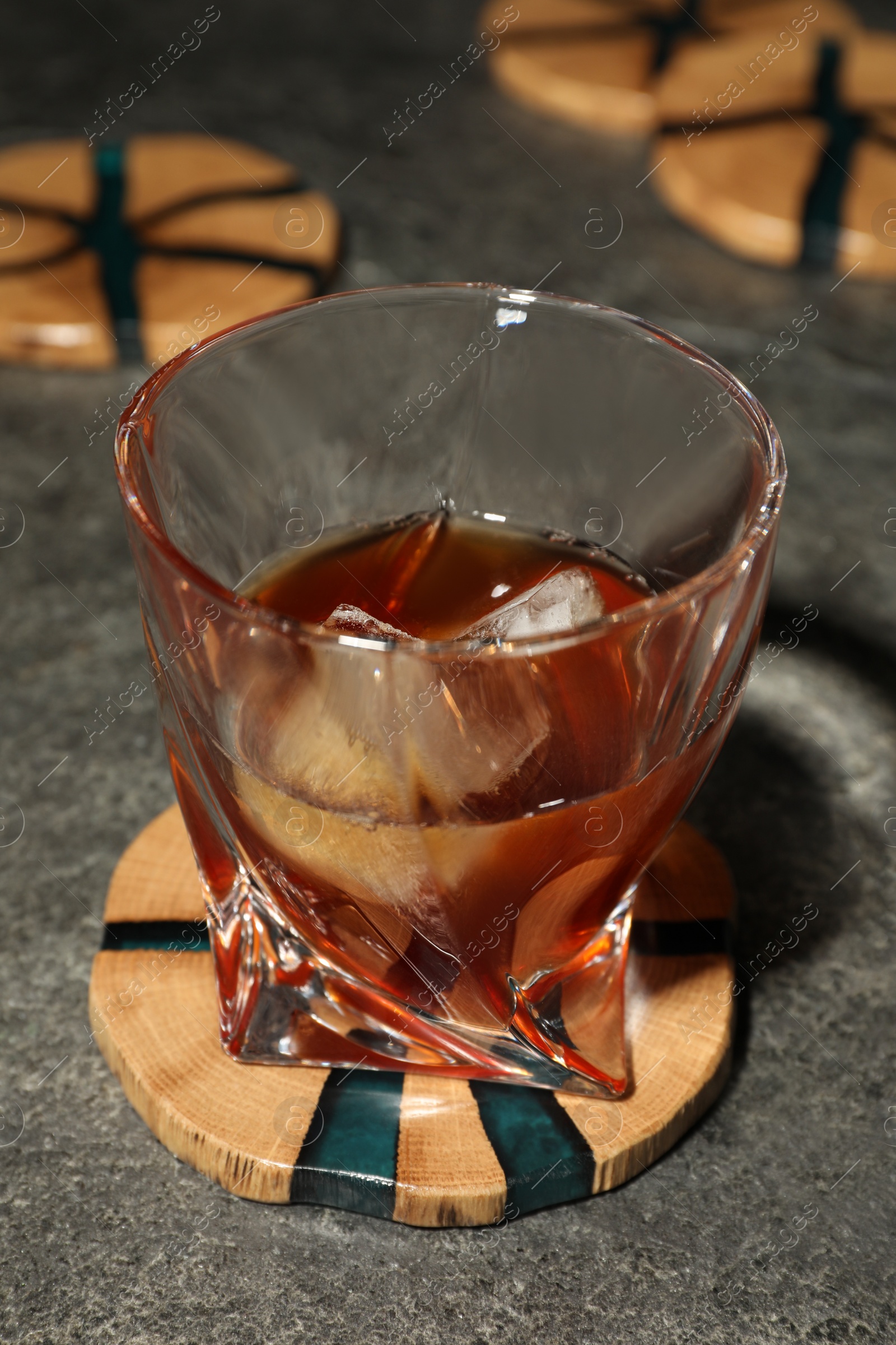 Photo of Glass of cold drink and stylish wooden cup coaster on grey table