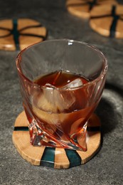 Glass of cold drink and stylish wooden cup coaster on grey table