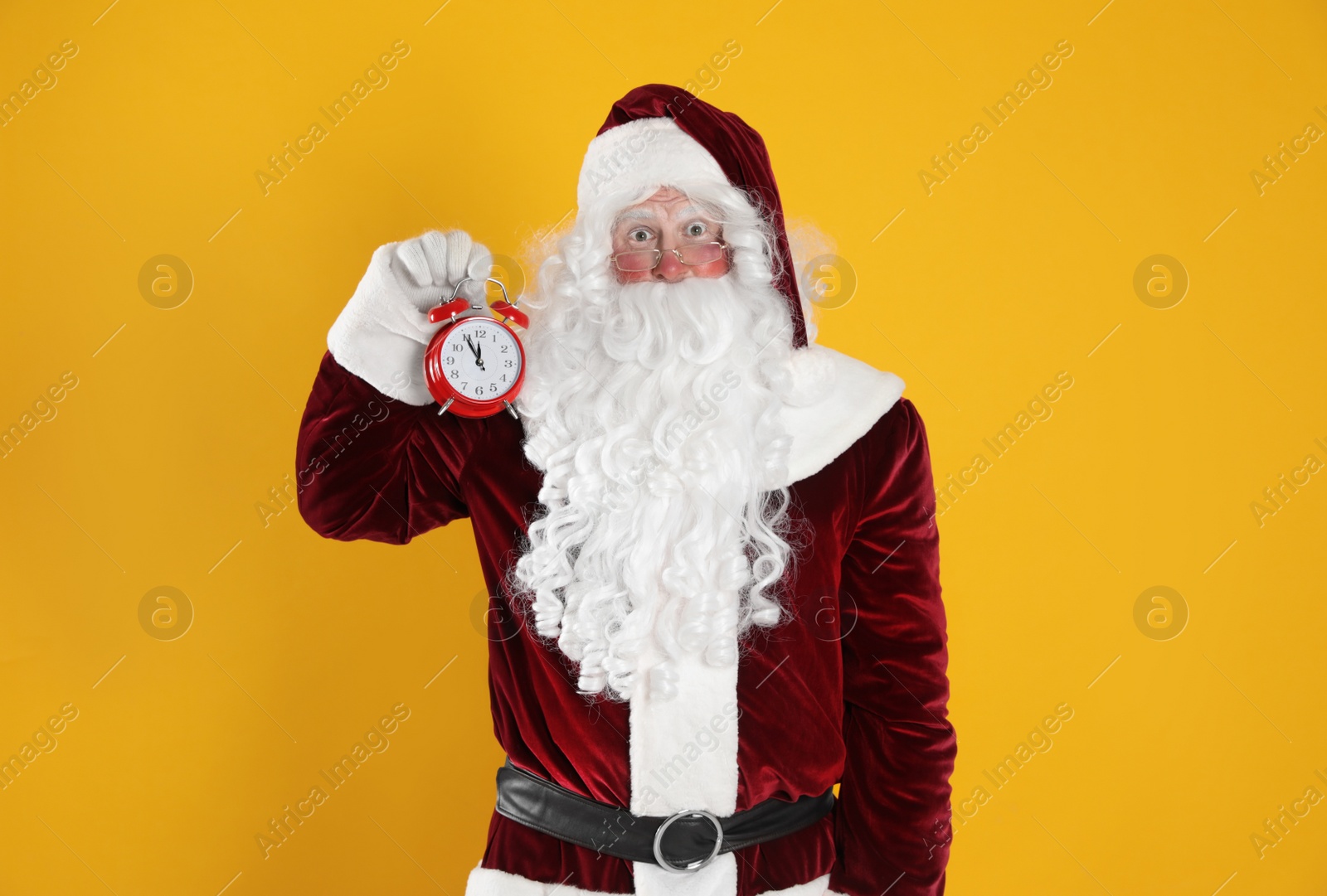 Photo of Santa Claus holding alarm clock on yellow background. Christmas countdown