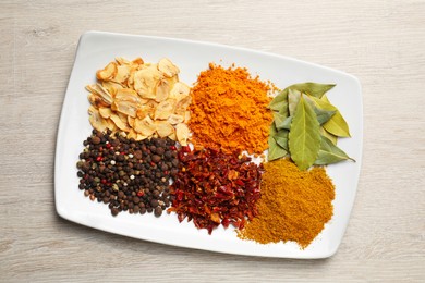 Plate with different spices on light table, top view
