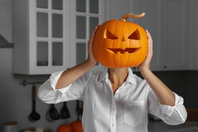 Photo of Woman holding carved pumpkin for Halloween in kitchen