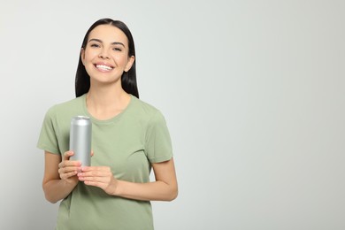 Beautiful happy woman holding beverage can on light grey background. Space for text