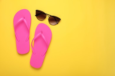 Photo of Stylish pink flip flops and sunglasses on yellow background, flat lay. Space for text