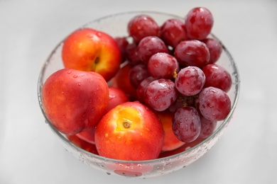 Photo of Glass bowl with fresh grapes and nectarines on white table, closeup