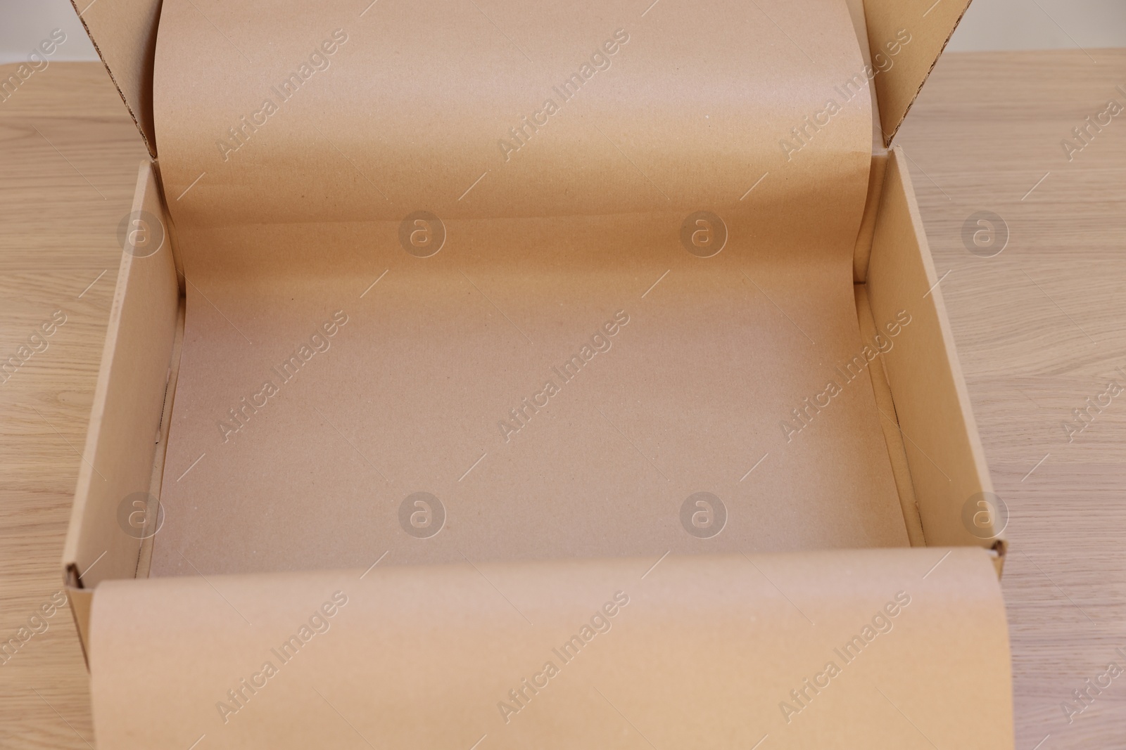 Photo of Empty cardboard box with kraft paper on wooden table. Delivery service