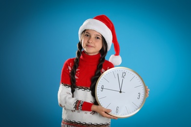Photo of Girl in Santa hat with clock on light blue background. New Year countdown