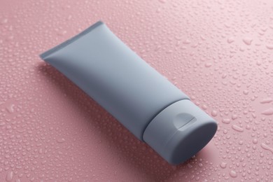 Photo of Moisturizing cream in tube on pink background with water drops, closeup
