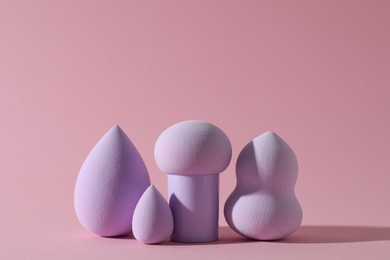 Photo of Many violet makeup sponges on pink background