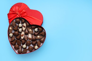 Photo of Heart shaped box with delicious chocolate candies on light blue background, top view. Space for text