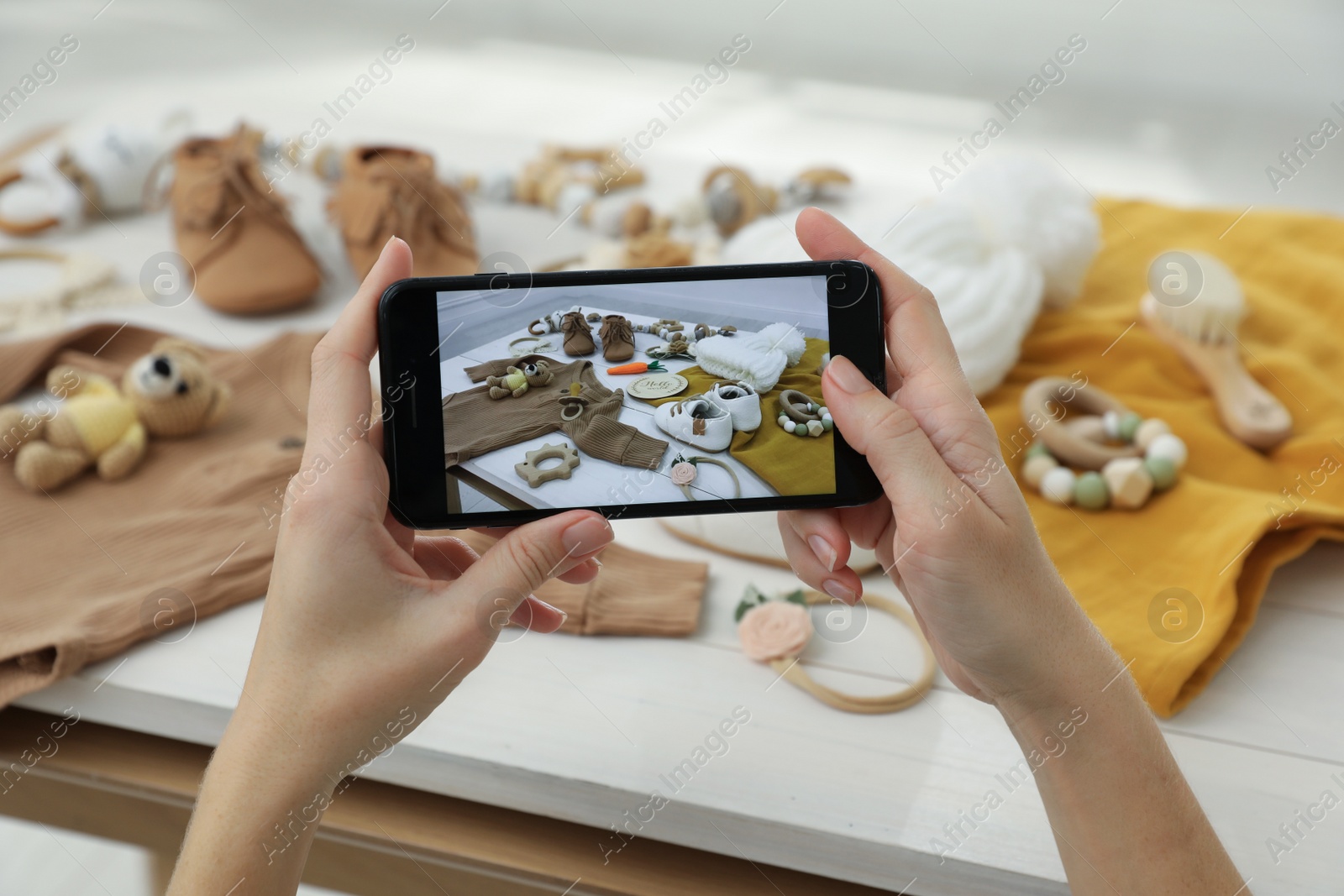 Photo of Woman taking picture of baby clothes at white wooden table, closeup