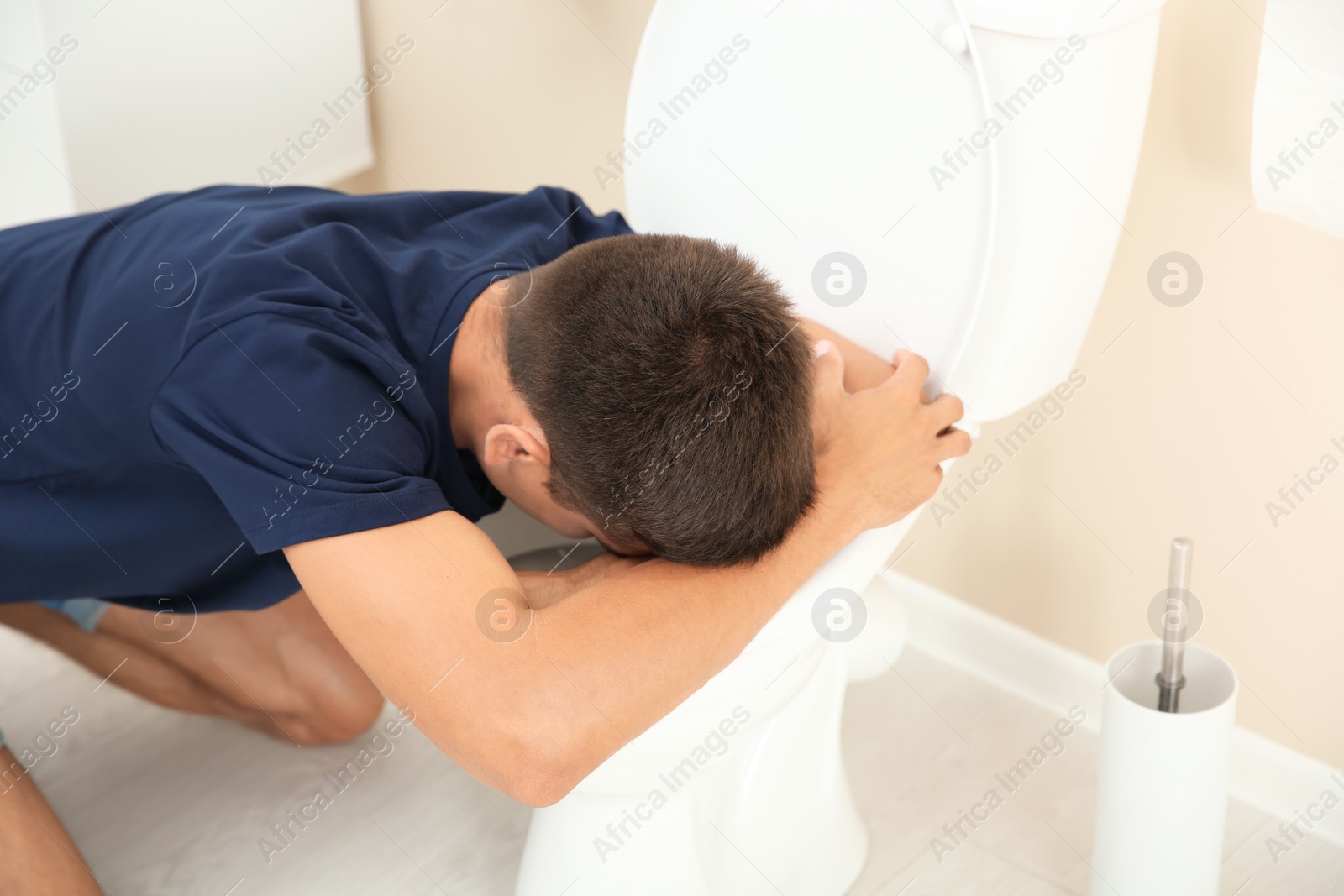 Photo of Young man vomiting in toilet bowl at home