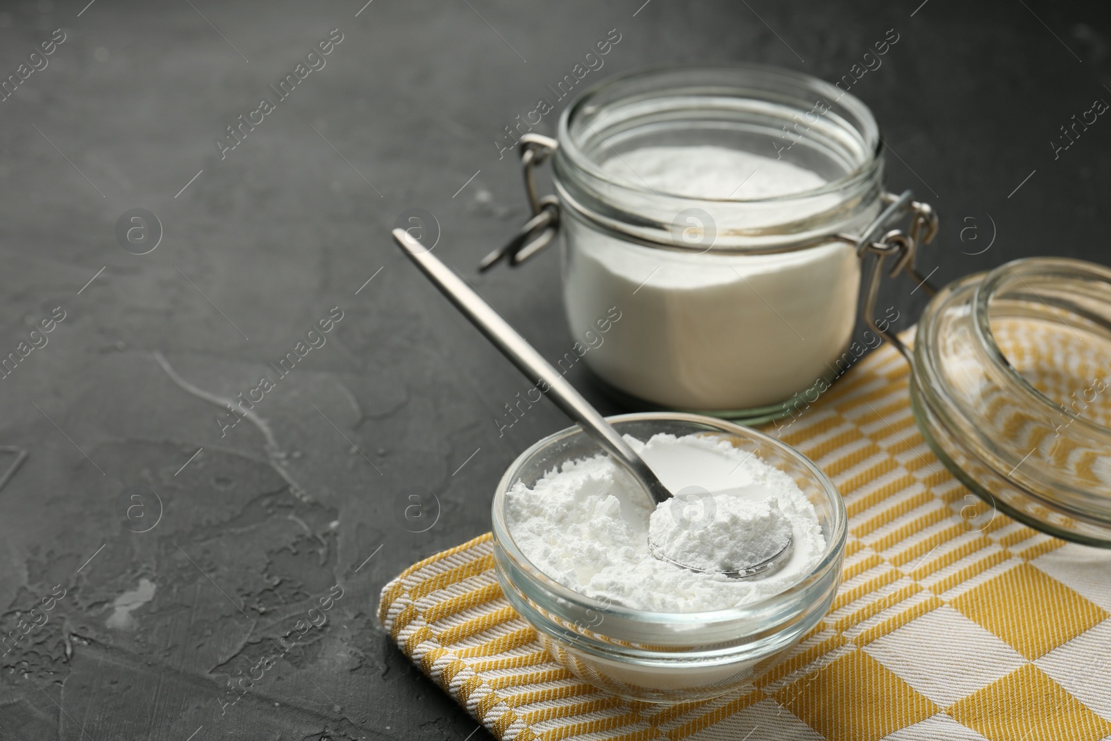 Photo of Baking powder in bowl, jar and spoon on black textured table, closeup. Space for text