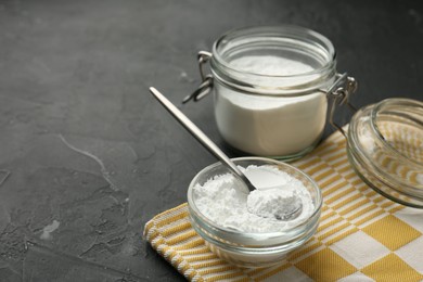 Baking powder in bowl, jar and spoon on black textured table, closeup. Space for text