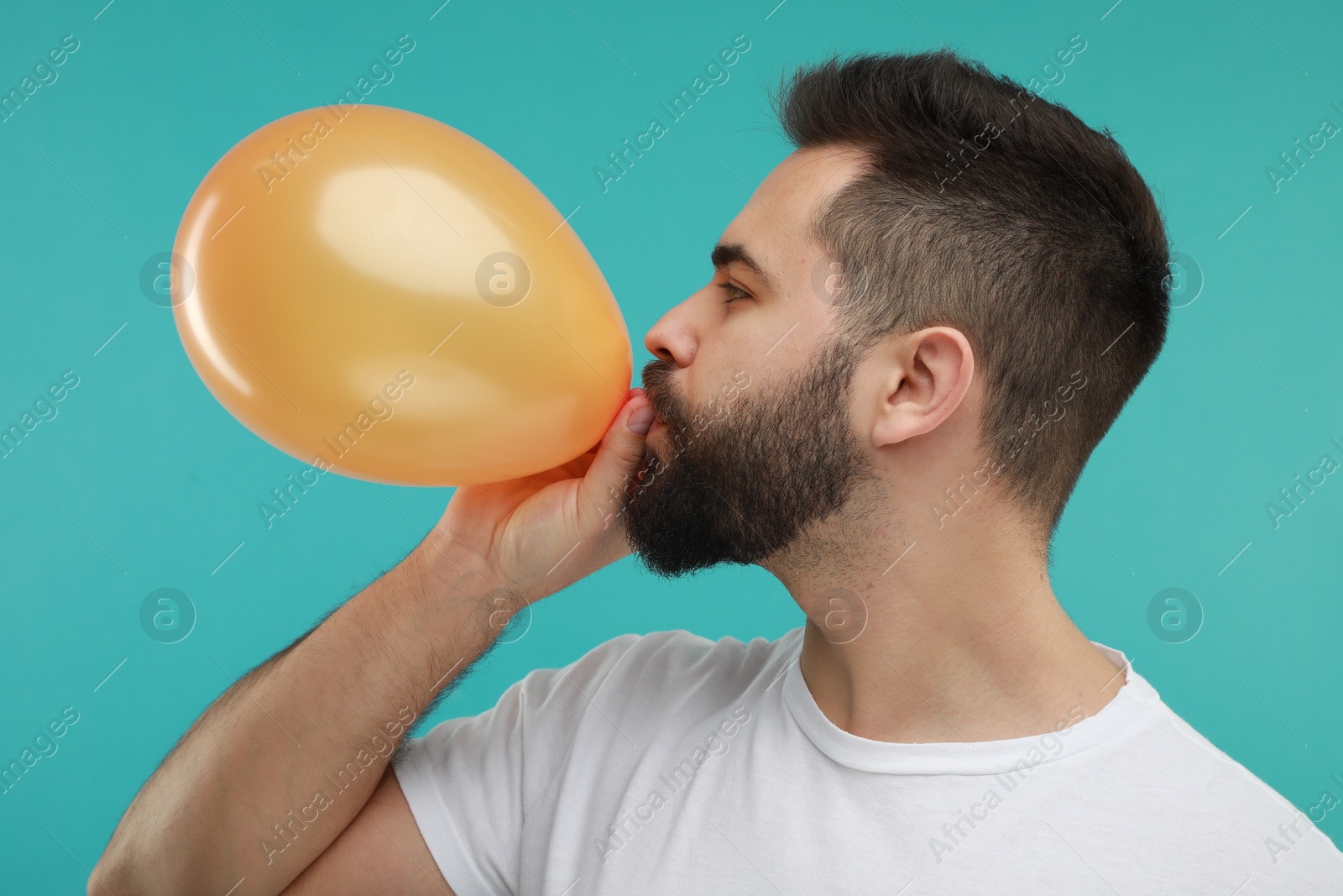 Photo of Man inflating bright balloon on turquoise background