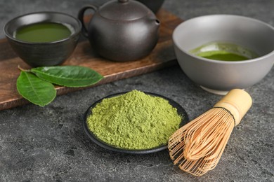 Green matcha powder, bamboo whisk and fresh beverage on grey table, closeup