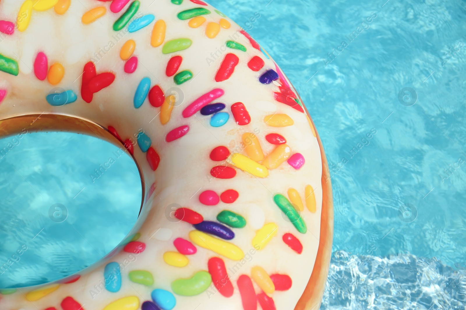 Photo of Bright inflatable doughnut ring floating in swimming pool on sunny day. Space for text