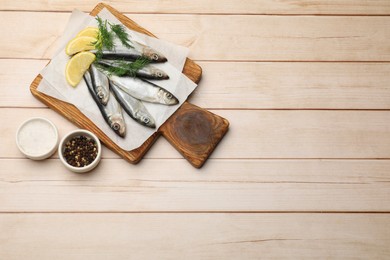 Photo of Fresh raw sprats, lemon and dill on light wooden table, top view. Space for text