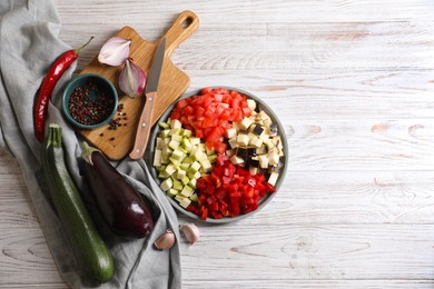 Photo of Cooking delicious ratatouille. Fresh ripe vegetables, plate and knife on white wooden table, flat lay. Space for text