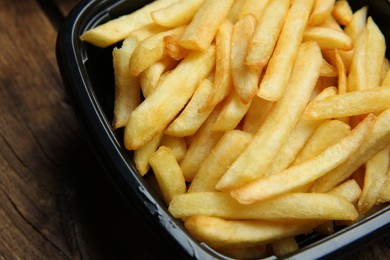 Photo of Container with French fries on wooden table, closeup. Food delivery service