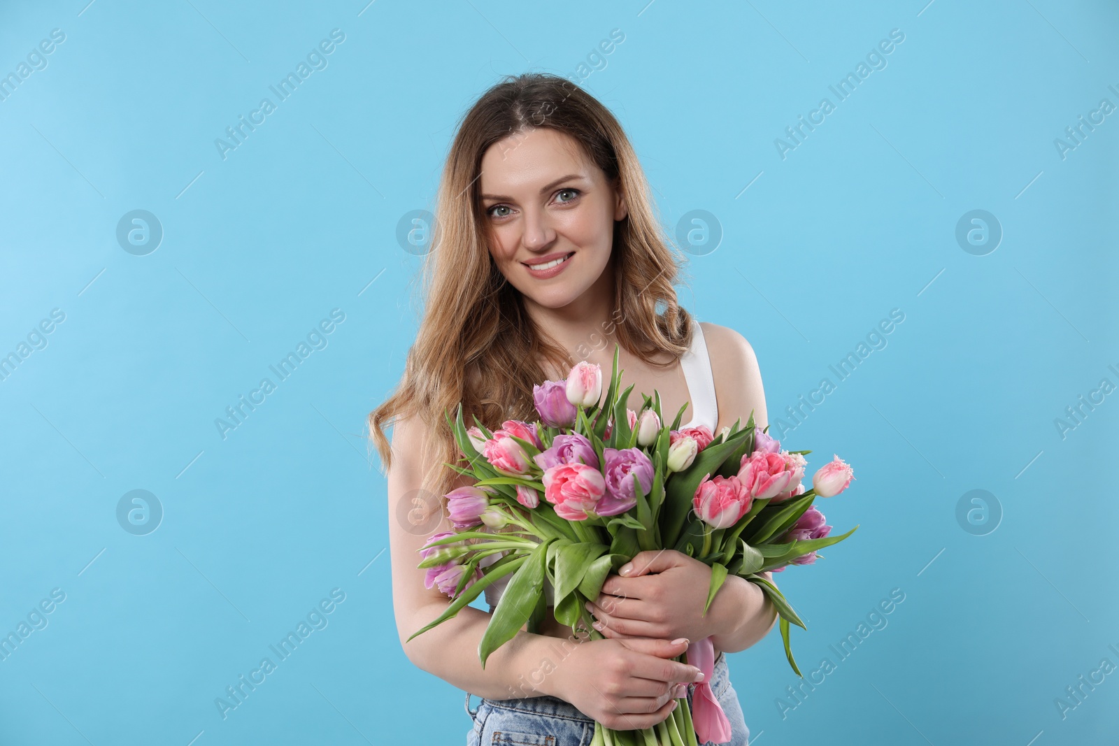 Photo of Happy young woman with bouquet of beautiful tulips on light blue background