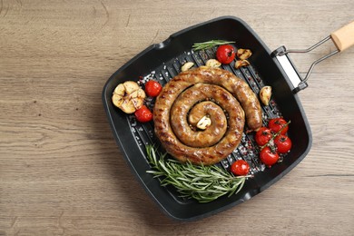 Photo of Delicious homemade sausage with garlic, tomatoes, rosemary and spices in grill pan on wooden table, top view. Space for text