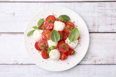 Photo of Tasty salad Caprese with tomatoes, mozzarella balls and basil on white wooden table, top view
