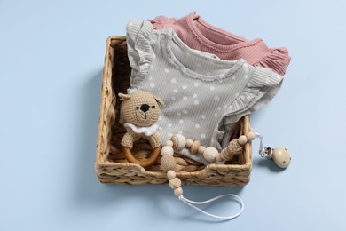 Different baby accessories and clothes in wicker box on light blue background, top view