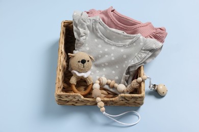 Photo of Different baby accessories and clothes in wicker box on light blue background, top view