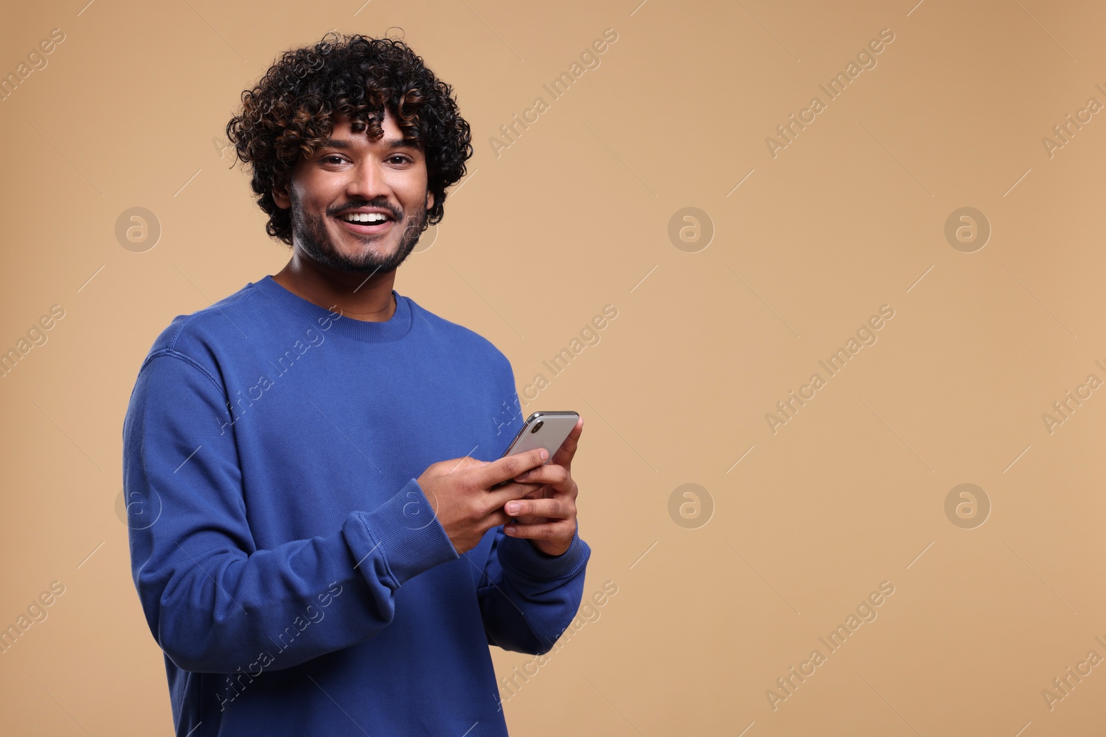 Photo of Handsome smiling man using smartphone on beige background, space for text